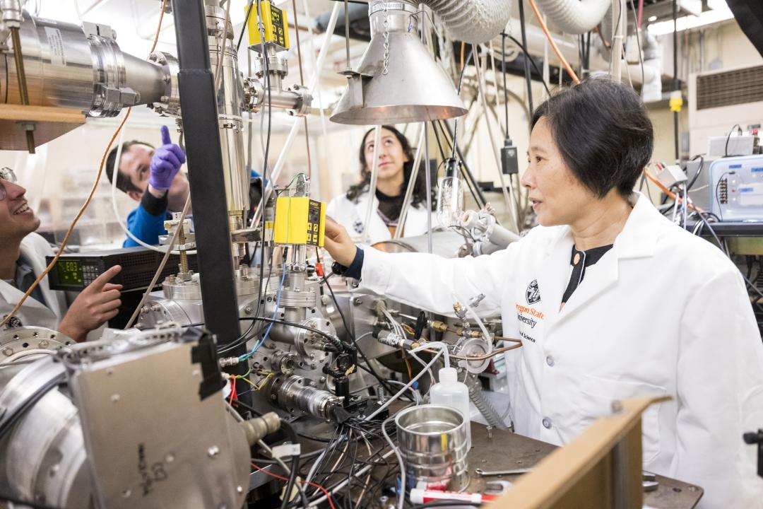 Wei Kong and graduate students work in the lab on a huge machine with wires.