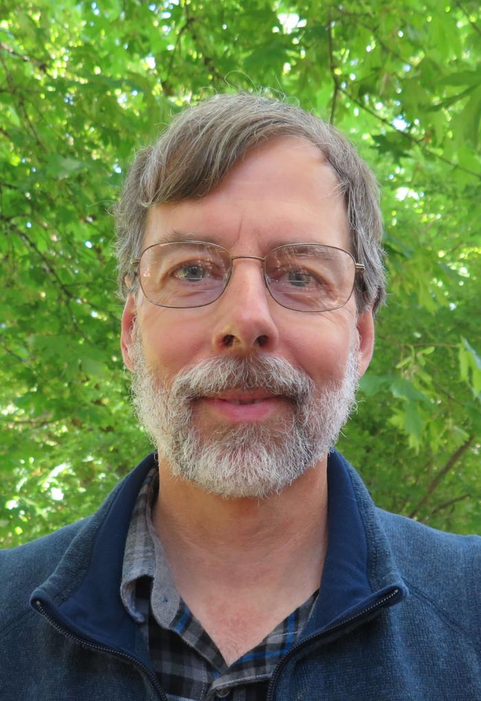 man wearing glasses standing in front of a tree