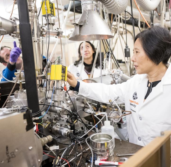 Wei Kong and graduate students work in the lab on a huge machine with wires.